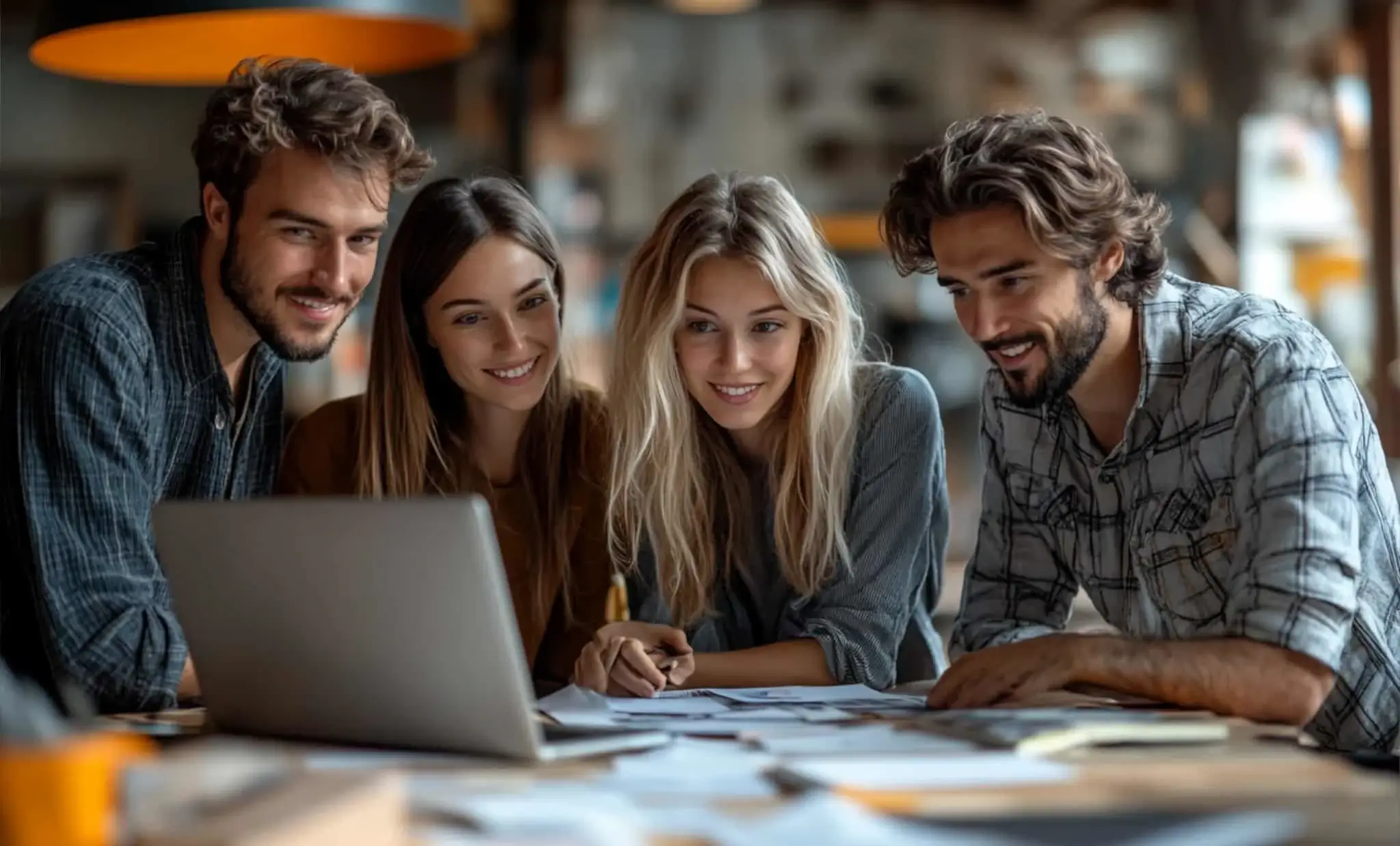 Grupa czterech młodych profesjonalistów pracuje wspólnie przy laptopie, analizując dane i modernizując stronę internetową